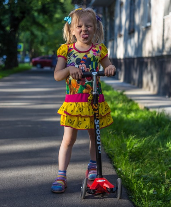 child on a three wheeled scooter making a funny face