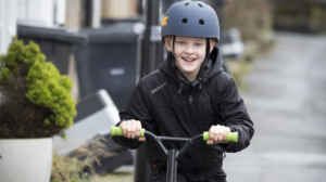 kid in a black jacket riding his black scooter